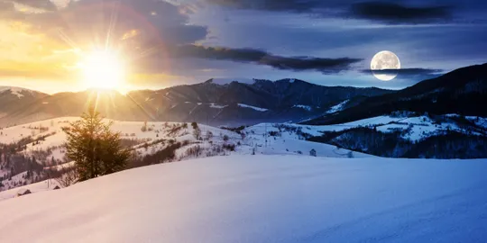 Sunset and moon over snowy landscape